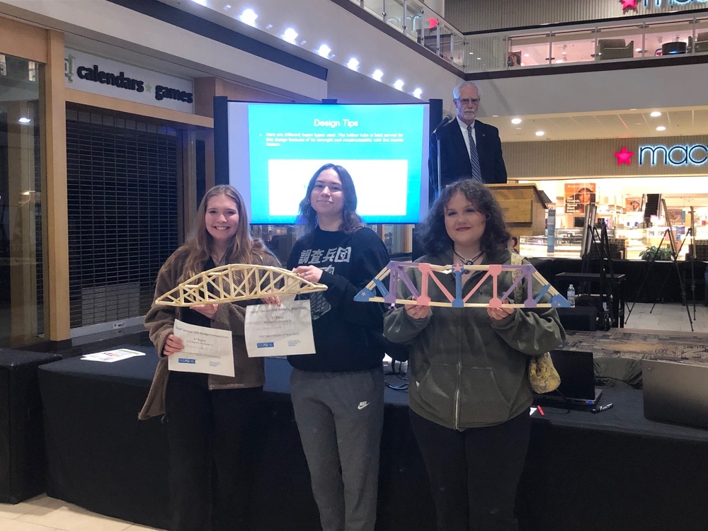 three students holding bridges from bridge design contest