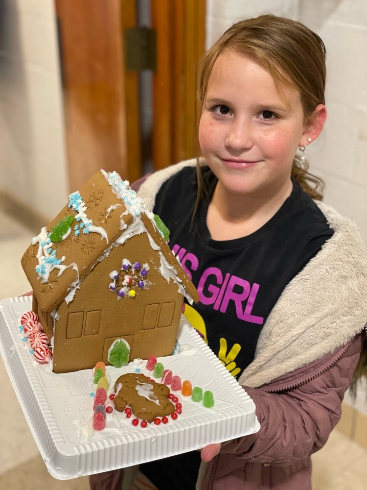 student smiling holding gingerbread house 